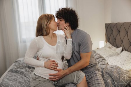 Téléchargez les photos : Heureux couple enceinte en amour profiter tout en se relaxant sur un lit dans la chambre. - en image libre de droit
