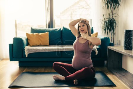 Foto de Mujer embarazada joven haciendo ejercicio en casa. Ella entrena en la esterilla de ejercicio y estiramiento. - Imagen libre de derechos
