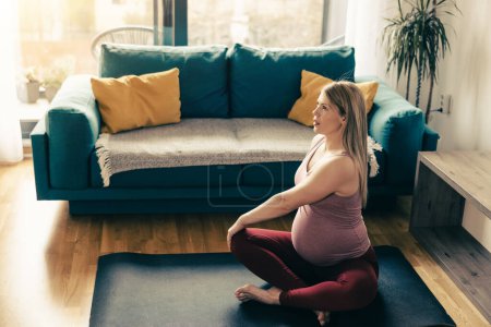 Photo for Young pregnant woman exercising at home. She workout on exercise mat and stretching in her living room. - Royalty Free Image