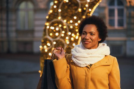 Foto de Hermosa mujer negra sonriente caminando y comprando durante las vacaciones de Navidad en la ciudad. - Imagen libre de derechos
