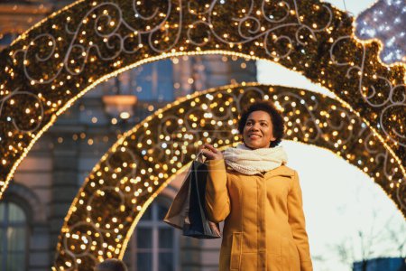 Téléchargez les photos : Belle femme noire souriante marchant et faisant du shopping pendant les vacances de Noël dans la ville. - en image libre de droit