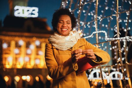 Photo for Middle age black woman holding sparklers at festive winter night in the city. - Royalty Free Image