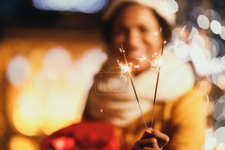 Photo for Selectiv focus of an African woman holding sparklers at Christmas festive night in the city. - Royalty Free Image