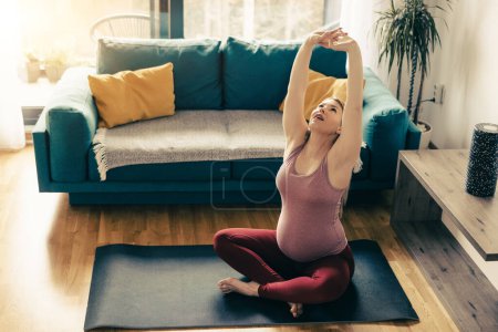 Photo for Young pregnant woman exercising at home. She workout on exercise mat and stretching in her living room. - Royalty Free Image