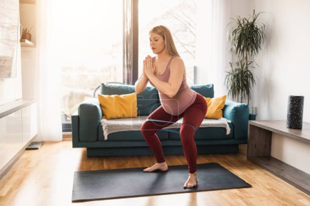 Téléchargez les photos : Jeune femme enceinte faisant de l'exercice avec élastique à la maison le matin. - en image libre de droit