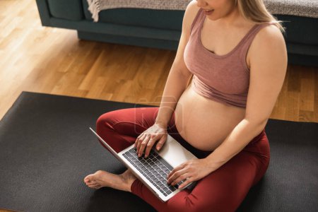 Photo for Shot of an unrecognisable pregnant woman using laptop while exercising yoga at home. She relaxing on exercise. - Royalty Free Image