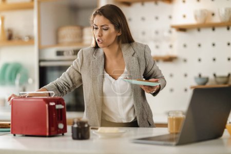 Téléchargez les photos : Prise de vue d'une jeune femme d'affaires multi-tâches prenant un petit déjeuner à la maison tout en se préparant à aller au travail. - en image libre de droit