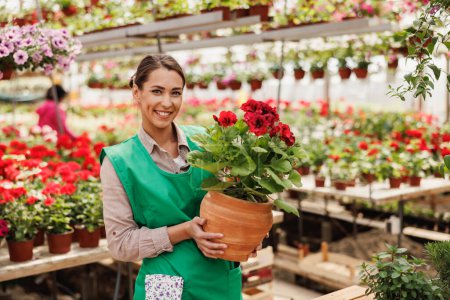 Foto de Retrato de una hermosa florista joven sosteniendo maceta en un centro de jardín. Mujer emprendedora mirando la cámara. - Imagen libre de derechos