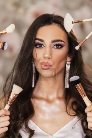 Photo for A portrait of a beautiful young woman surrounded by makeup brushes who is presenting a nice makeup on her face. - Royalty Free Image