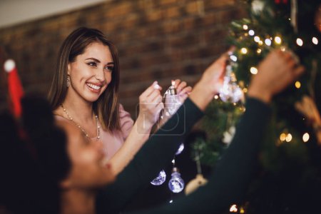 Foto de Hermosas amigas multiétnicas disfrutando de las vacaciones, decorando el árbol de Navidad, arreglando las luces de Navidad y divirtiéndose. - Imagen libre de derechos