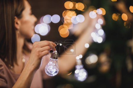 Téléchargez les photos : Belle jeune femme décorer sa maison avec des ampoules de Noël et profiter du temps des vacances. - en image libre de droit