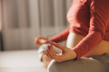 Téléchargez les photos : Gros plan d'une femme enceinte méconnaissable faisant des exercices de méditation de yoga en position lotus sur un lit dans la chambre. - en image libre de droit