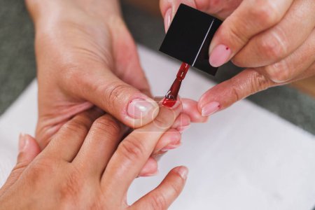 Téléchargez les photos : Image recadrée d'un esthéticien méconnaissable appliquant du vernis à ongles rouges à une femme lors d'un traitement de manucure dans un salon de beauté. - en image libre de droit