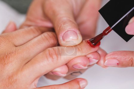 Foto de Imagen recortada de una esteticista irreconocible aplicando esmalte de uñas rojas a la mujer durante el tratamiento de manicura en un salón de belleza. - Imagen libre de derechos