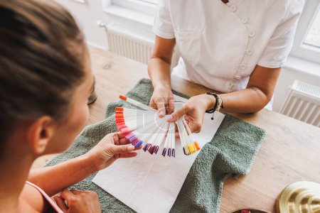 Téléchargez les photos : Image recadrée d'une femme choisissant la couleur des ongles pendant le traitement de manucure dans un salon de beauté. - en image libre de droit