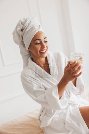 Téléchargez les photos : Belle jeune femme portant peignoir et serviette de tête avant le traitement spa dans un salon de beauté. - en image libre de droit