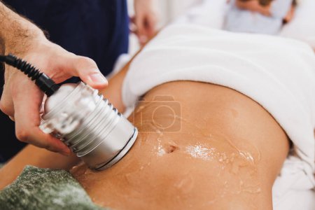 Photo for Unrecognizable woman getting an an ultrasound cavitation treatment to fat reduction on abdomen at the beauty salon. - Royalty Free Image
