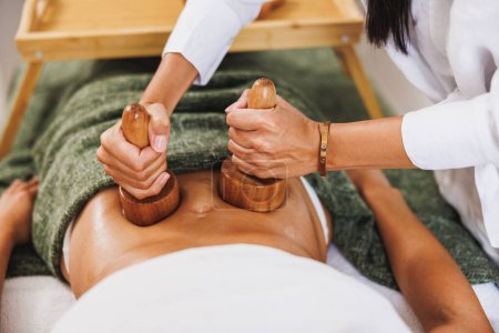 Téléchargez les photos : Une femme méconnaissable obtenant un massage anti-cellulite madérothérapie avec des tasses en bois au salon de beauté. - en image libre de droit