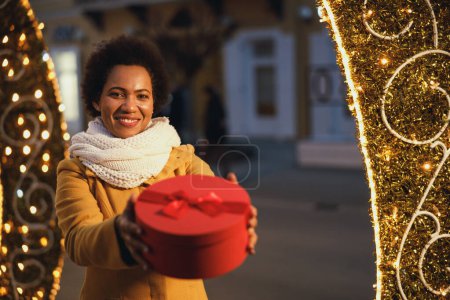 Téléchargez les photos : Femme noire du Moyen Âge à la nuit de fête dans la ville tenant cadeau sur le marché de Noël en plein air en hiver. - en image libre de droit