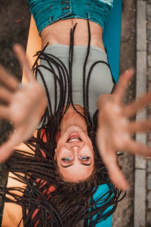 Photo for Cheerful caucasian young woman with long afro braids having fun while lying down on the colorful bench in the park. - Royalty Free Image
