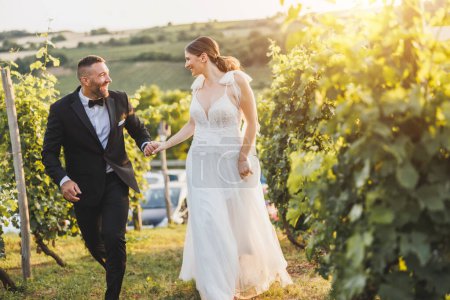Foto de Foto de una feliz pareja joven divirtiéndose y corriendo en el viñedo al atardecer en el día de su boda. - Imagen libre de derechos