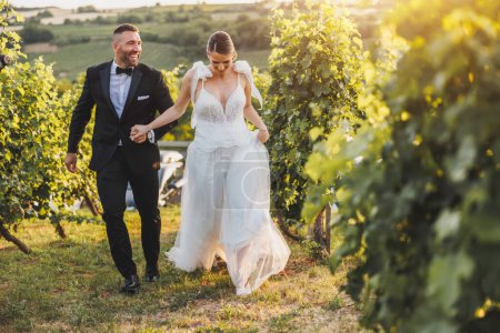 Foto de Foto de una alegre pareja divirtiéndose en el viñedo al atardecer en el día de su boda. - Imagen libre de derechos