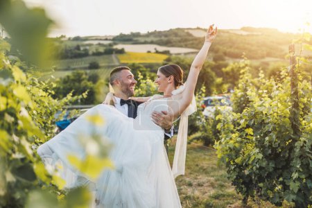 Téléchargez les photos : Joyeux marié portant et filant sa mariée tout en profitant dans la vigne le jour de leur mariage. - en image libre de droit