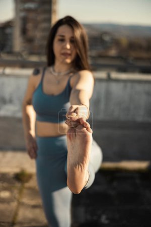 Téléchargez les photos : Young woman practicing yoga while doing training outdoors. Selective focus, focus on a woman's foot. - en image libre de droit