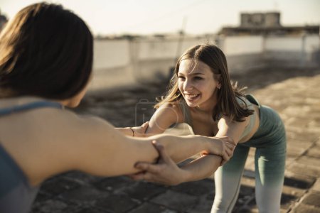 Téléchargez les photos : Two young women doing stretching yoga exercises on a rooftop terrace. - en image libre de droit
