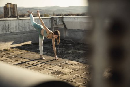 Photo for Female teenager practicing yoga on a rooftop terrace. - Royalty Free Image