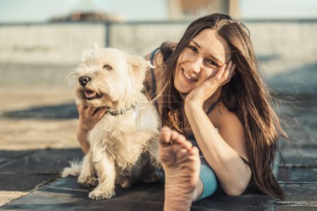 Téléchargez les photos : Femme détendue jouant avec ses animaux de compagnie de chien tout en pratiquant l'exercice d'étirement de yoga sur un toit-terrasse. - en image libre de droit