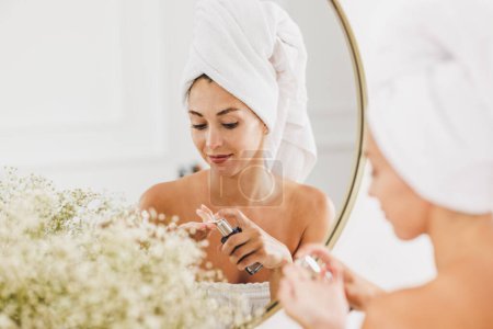 Téléchargez les photos : Jeune femme devant miroir passant par sa routine beauté matinale dans la salle de bain à la maison. - en image libre de droit