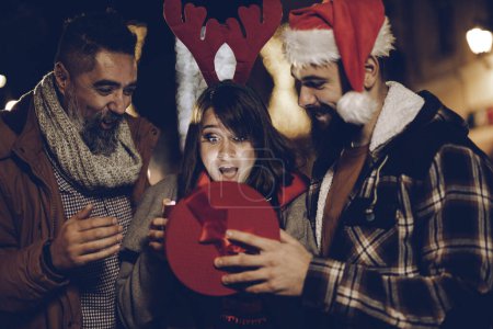 Téléchargez les photos : Tourné d'un trois joyeux jeunes amis regardant excité après avoir reçu un cadeau de Noël et s'amuser lors d'une soirée. - en image libre de droit