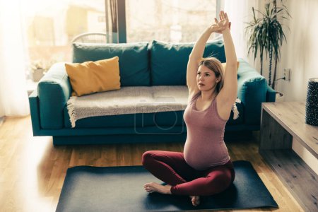 Photo for Young pregnant woman exercising yoga at home. She workout on exercise mat and stretching in her living room. - Royalty Free Image