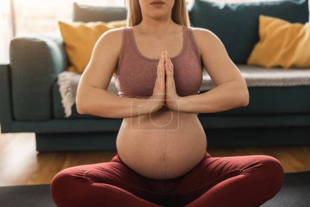 Téléchargez les photos : Prise de vue d'une femme enceinte méconnaissable faisant du yoga à la maison. Elle se relaxe sur un tapis d'exercice dans son salon. - en image libre de droit