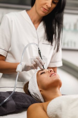 Téléchargez les photos : Tournage d'une belle jeune femme sur un traitement facial de microdermabrasion au salon de beauté. - en image libre de droit