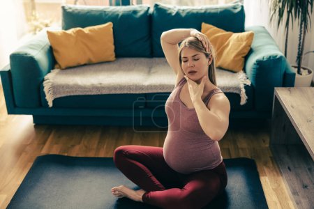 Photo for A pregnant woman in sports clothing is stretching and exercising yoga to promote wellbeing in her living room. - Royalty Free Image
