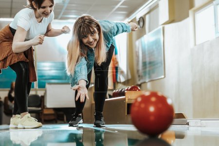 Téléchargez les photos : Deux jeunes femmes souriantes s'amusent tout en lançant la boule de bowling et en passant du temps ensemble. - en image libre de droit