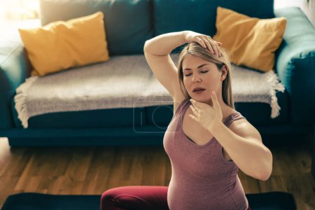 Photo for Young pregnant woman practicing yoga at home in the morning. She is doing stretching exercise in her living room. - Royalty Free Image