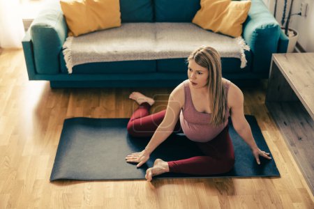 Photo for Young pregnant woman exercising mobility at home. She workout on exercise mat and stretching. - Royalty Free Image