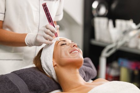 Téléchargez les photos : Tournage d'une belle jeune femme sur un dermapen facial traitement micro-aiguille au salon de beauté. - en image libre de droit