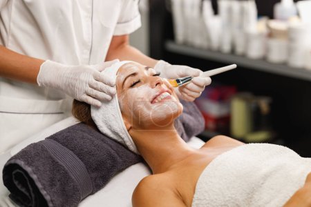 Téléchargez les photos : Tournage d'une belle jeune femme recevant un traitement de masque facial au salon de beauté. - en image libre de droit