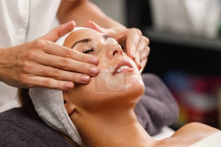 Téléchargez les photos : Tournage d'une belle jeune femme bénéficiant d'un massage du visage au salon de beauté. - en image libre de droit