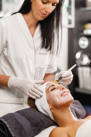Téléchargez les photos : Tournage d'une belle jeune femme recevant un traitement de masque facial au salon de beauté. - en image libre de droit
