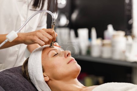 Téléchargez les photos : Tournage d'une belle femme mature sur un traitement facial de microdermabrasion au salon de beauté. - en image libre de droit