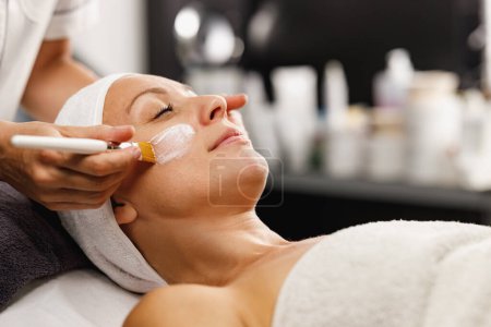 Photo for Shot of a beautiful mature woman getting a facial mask treatment at the beauty salon. - Royalty Free Image