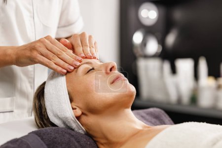 Téléchargez les photos : Tournage d'une belle femme mature bénéficiant d'un massage du visage au salon de beauté. - en image libre de droit