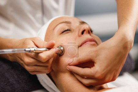 Téléchargez les photos : Tournage d'une belle femme mature sur un traitement facial de microdermabrasion au salon de beauté. - en image libre de droit