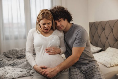 Foto de Hombre preocupado consolando a su esposa embarazada en un dormitorio - Imagen libre de derechos