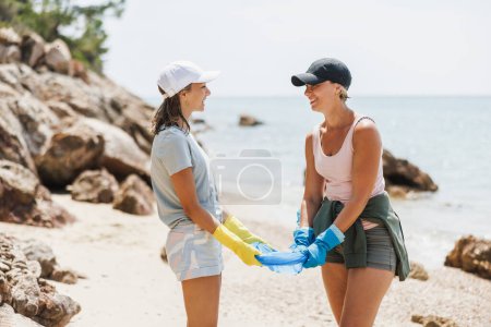 Foto de Mamá y su hija son voluntarias compartiendo bolsas de basura y preparándose para limpiar la playa del mar. - Imagen libre de derechos